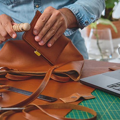 Craftsman burnishing edges of leather bag in his workshop